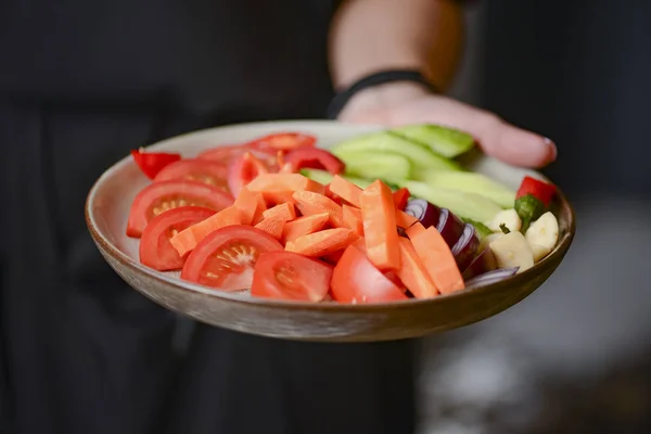 Waiter holds a plate of tasty food, mixed vegetables on a plate. Carrots, cucumbers, tomatoes