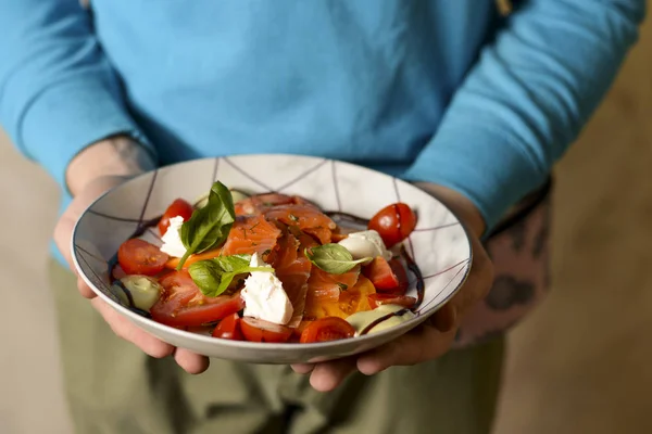 Um garçom segura um prato de comida saborosa. Cozinha italiana no restaurante, Salada com peixe de salmão, queijo feta, tomates — Fotografia de Stock