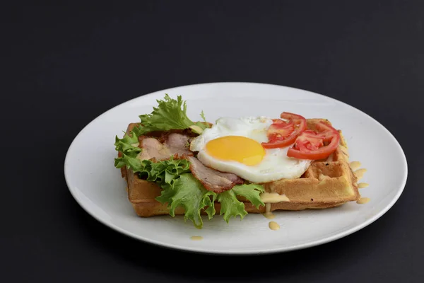 Œufs classiques et viande de bacon sur gaufres petit déjeuner avec tomates et salade servi sur une assiette blanche sur fond noir . — Photo