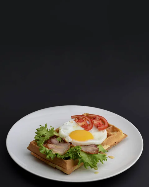 Œufs classiques et viande de bacon sur gaufres petit déjeuner avec tomates et salade servi sur une assiette blanche sur fond noir . — Photo