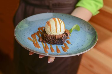 Garson restoranda yemek servisi yapıyor. Vanilyalı çikolatalı kek ve mavi tabakta çikolata sosu..