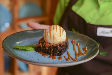 Garson restoranda yemek servisi yapıyor. Vanilyalı çikolatalı kek ve mavi tabakta çikolata sosu..
