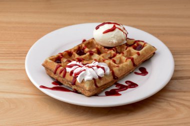 Bir tabak Belçika waffle 'ı dondurma ve ahşap masa arkasında çilekli karamel sosu.