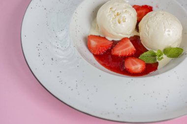 Çilekli vanilyalı çilekli dondurma ve pastel pembe arka planda beyaz bir tabakta meyve şurubu. Üst görünüm.