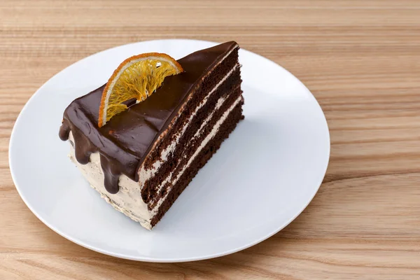 Um pedaço de bolo de chocolate delicioso cozido no forno fresco decorado com laranjas cristalizadas no topo sobre fundo de madeira leve — Fotografia de Stock