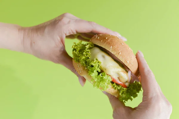 Hand holding a burger on a bright green background. Eating and healthy concept, restaurant food concept. — 스톡 사진