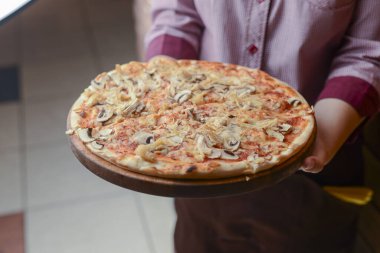 Garson bir tabak lezzetli yemek tutuyor. Restoranda İtalyan mutfağı. Tavuk etli, mantarlı, sosisli lezzetli pizza..