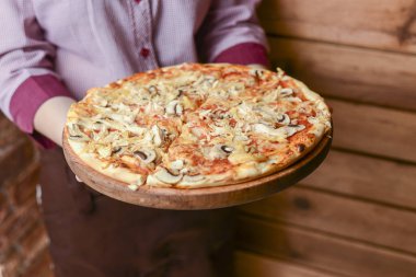 Garson bir tabak lezzetli yemek tutuyor. Restoranda İtalyan mutfağı. Tavuk etli, mantarlı, sosisli lezzetli pizza..