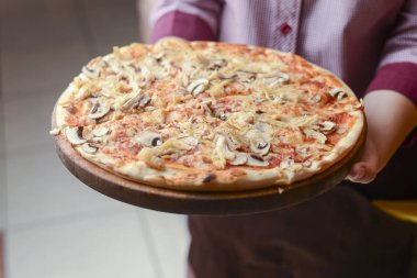 Garson bir tabak lezzetli yemek tutuyor. Restoranda İtalyan mutfağı. Tavuk etli, mantarlı, sosisli lezzetli pizza..