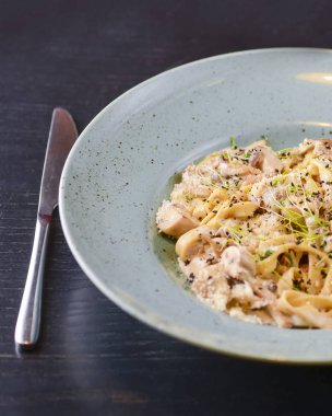 Beyaz tabakta servis edilen geleneksel İtalyan makarnası, kirazlı domates, parmezan peyniri ve maydanoz.