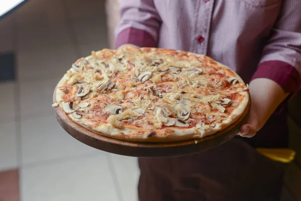 Garson bir tabak lezzetli yemek tutuyor. Restoranda İtalyan mutfağı. Tavuk etli, mantarlı, sosisli lezzetli pizza..