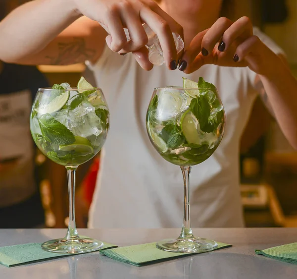 Barmans Hand verziert zwei Gläser mit alkoholischen Cocktailgetränken, die in einer Reihe angeordnet sind. Barkeeper bei der Arbeit in Bar. — Stockfoto