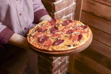 Garson bir tabak lezzetli yemek tutuyor. Restoranda İtalyan mutfağı. Tavuk etli, mantarlı, sosisli lezzetli pizza..