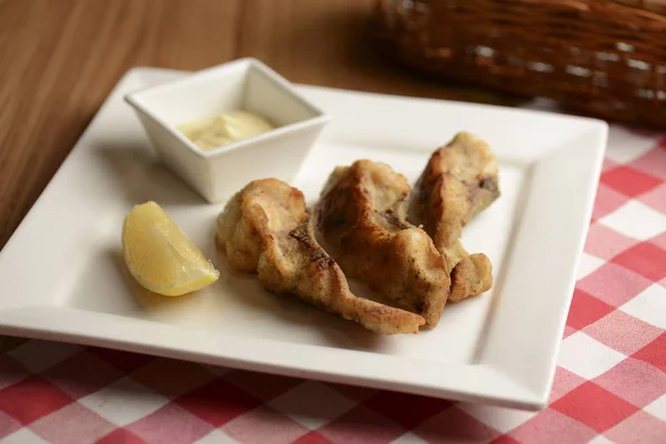 Fried fish with lemon and sauce served on white plate over wooden table with plaid tablecloth in restaurant. — Stockfoto