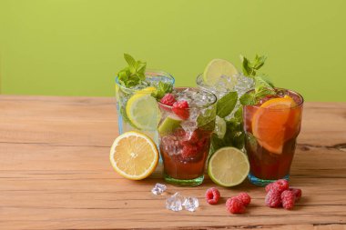 Dört tropikal karışık içki, portakal, limon ve ahududu kokteyli parlak pastel yeşil arka plan üzerine.