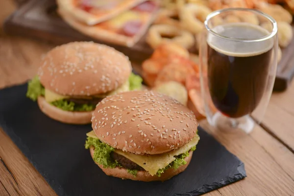Dwa hamburgery, cola i inne fast food na rustykalnym drewnianym stole. Fast food, koncepcja fast food. — Zdjęcie stockowe