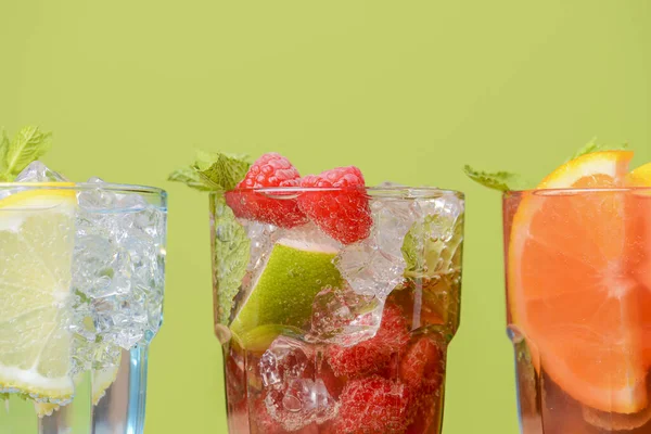 Três bebidas tropicais mistas, coquetéis de laranja, limão e framboesas sobre fundo verde pastel brilhante . — Fotografia de Stock