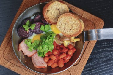 Geleneksel Tam İngiliz Kahvaltısı. Kızarmış yumurta, sosis, fasulye, mantar ve pastırma kızartma tavasında.