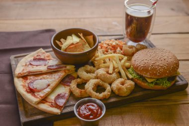 Fast food concept with greasy fried onion rings, burgers, and pizza with french fries and popcorn. Junk food concept. clipart