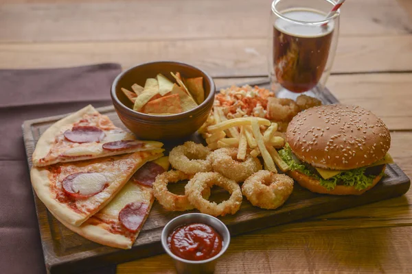 Fast food concept με λαδερά τηγανητά onion rings, burgers και πίτσα με τηγανητές πατάτες και ποπ κορν. Έννοια πρόχειρου φαγητού. — Φωτογραφία Αρχείου