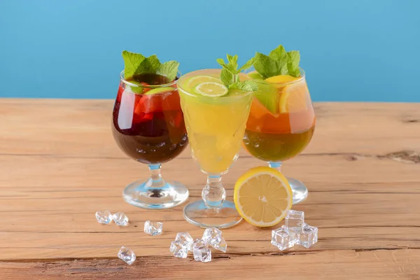 Three tropical mixed drinks with lime and lemon and mint leaves served in different glasses on rustic wooden table.