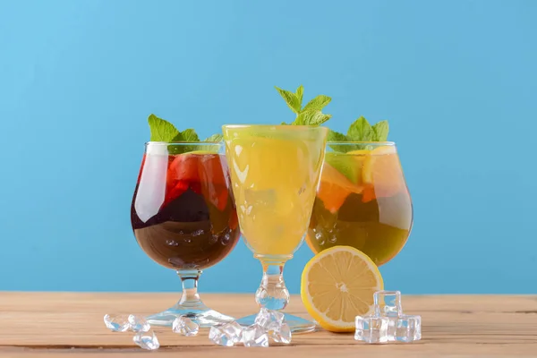 Trzy tropikalne napoje zmieszane z limonką, cytryną i liśćmi mięty serwowane w różnych szklankach na drewnianym stole rustykalnym. — Zdjęcie stockowe