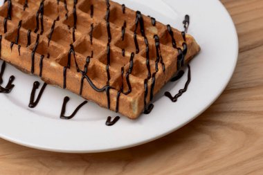 Tahta masa arkasında çikolatalı karamel soslu Belçika waffle tabağı. Geleneksel Belçika mutfağı, tatlı.