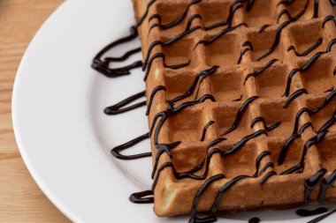 Tahta masa arkasında çikolatalı karamel soslu Belçika waffle tabağı. Geleneksel Belçika mutfağı, tatlı.