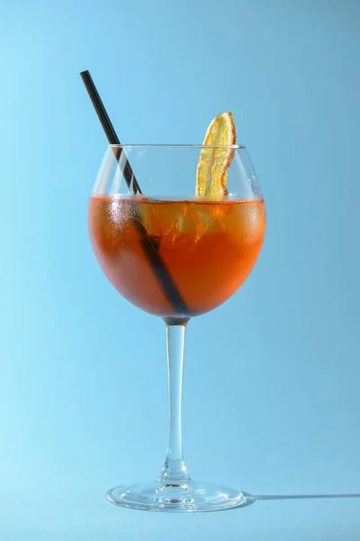 Ein Glas Obstlikör im Weinglas mit einem Stück Zitrone und schwarzem Plastikstroh isoliert auf pastellblauem Hintergrund. — Stockfoto