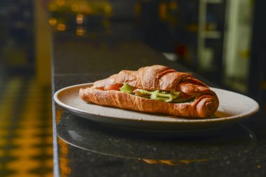 Restoranda ya da kafede beyaz tabakta servis edilen jambon ve marulla dolu taze pişmiş kruvasan..