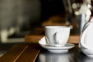 Siyah çaylı çay fincanı küçük bir tabakta, beyaz çaydanlık da siyah ahşap masada.