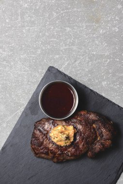 Orta pişmiş ızgara biftek ve siyah ahşap kesme tahtasında sos. Üst görünüm, kopyalama alanı, düz uzanma.