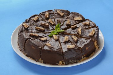 Salted caramel chocolate cake with nuts and vanilla decorated with chocolate pieces and mint leaf on blue background