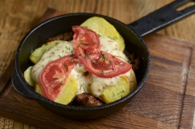 Meat and mushroom gratin with cheese and tomatoes served in a pan over dark wooden table background. Ukrainian cuisine.