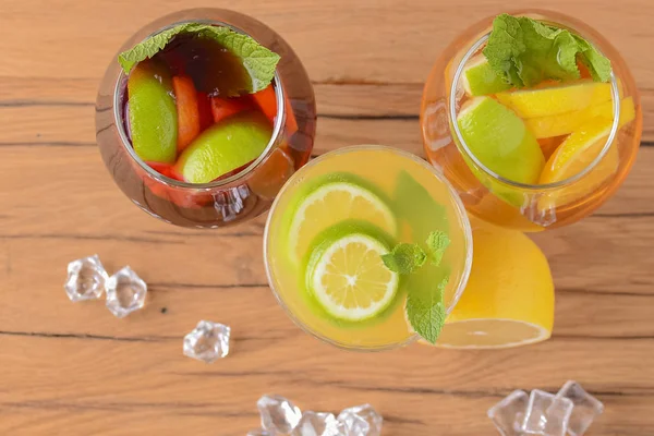 Trzy tropikalne napoje zmieszane z limonką, cytryną i liśćmi mięty serwowane w różnych szklankach na drewnianym stole rustykalnym. — Zdjęcie stockowe