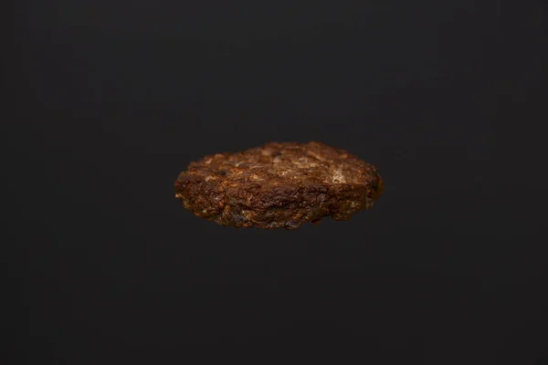 A thick, juicy hamburger patty cooked on a barbecue isolated on black background. Ingridients for making a hamburger.