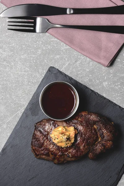 Bife grelhado médio raro com molho em tábua de corte de madeira preta com utensílios. Espaço de cópia, flat lay . — Fotografia de Stock