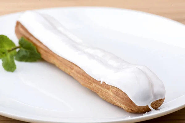 Traditionelle französische Nachspeise. leckeres Eclair mit Pudding und Schokoladenglasur auf einem weißen Teller mit Minzblatt. — Stockfoto