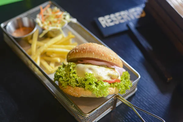 Burger with meat and french fries in aluminum tray on dark background with reserved sign on table. — Stock Photo, Image