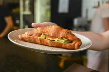 Restoranda ya da kafede beyaz tabakta servis edilen jambon ve marulla dolu taze pişmiş kruvasan..