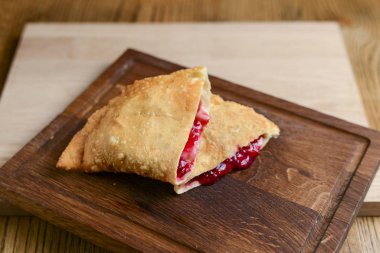 Koyu ahşap kesme tahtasının yatay üzerinde vişneli dilimlenmiş meyveli turta..