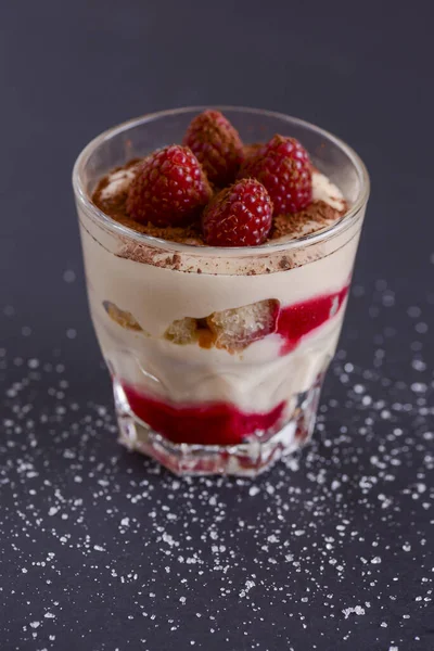 Italian dessert panna cotta with raspberries and cocoa powder served in small glass over black background. — Stock Photo, Image