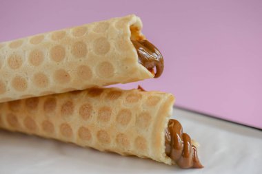 Pastel pembe arka planda beyaz tabakta kaynamış konsantre süt ile iki waffle konisi. Yoğunlaştırılmış borular.
