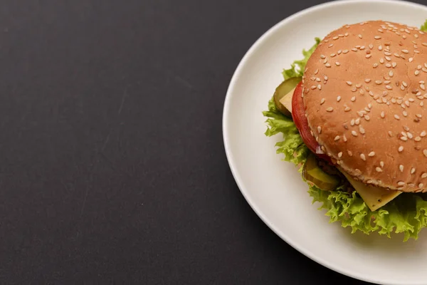 Klasyczny burger podawany na białym talerzu na czarnym tle. Mięsny hamburger płaski leżał. Jedzenie śmieciowe, koncepcja fast food. — Zdjęcie stockowe
