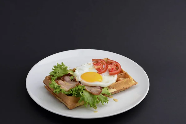 Œufs classiques et viande de bacon sur gaufres petit déjeuner avec tomates et salade servi sur une assiette blanche sur fond noir . — Photo