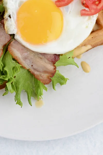 Класичні яйця та м'ясо бекону на вафельних сніданках з помідорами та салатом, поданими на білій тарілці на чорному тлі . — стокове фото