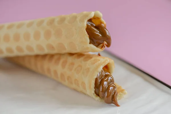 Two waffle cones with sweet boiled condensed milk in white plate on pastel pink background. Condensed tubules. — 스톡 사진