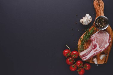 Taze çiğ biftek ahşap kesim tahtasında siyah arka planda baharatlarla, üst manzara.