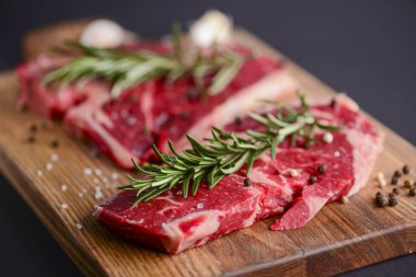 Ahşap kesme tahtasında taze çiğ biftek, siyah arka planda baharatlar, üst manzara..