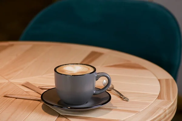 Fekete csésze kávé fekete tányérral és kanállal egy fa asztalon egy kávézóban vagy étteremben. — Stock Fotó